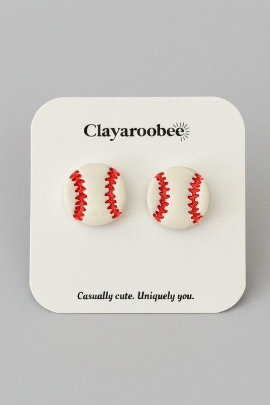 A pair of baseball stud earrings on a white display card with the brand name Clayaroobee