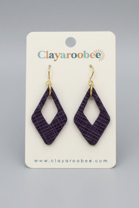 A pair of purple textured geometric dangle earrings with gold hooks, displayed on a white card labeled Clayaroobee
