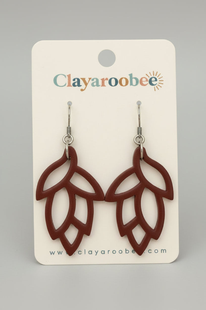 A pair of brown leaf-shaped dangle earrings displayed on a white Clayaroobee backing card