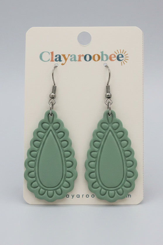 A pair of mint green clay earrings with a scalloped teardrop shape, displayed on a white Clayaroobee card.