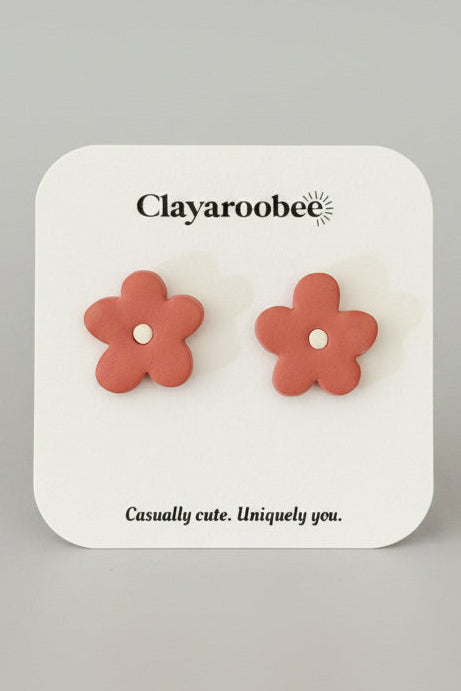 A pair of coral pink flower-shaped stud earrings displayed on a white brand card labeled 'Clayaroobee' 
