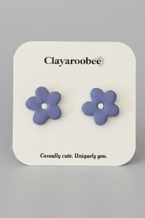 A pair of lavender purple flower-shaped stud earrings on a white display card with the brand name 'Clayaroobee'