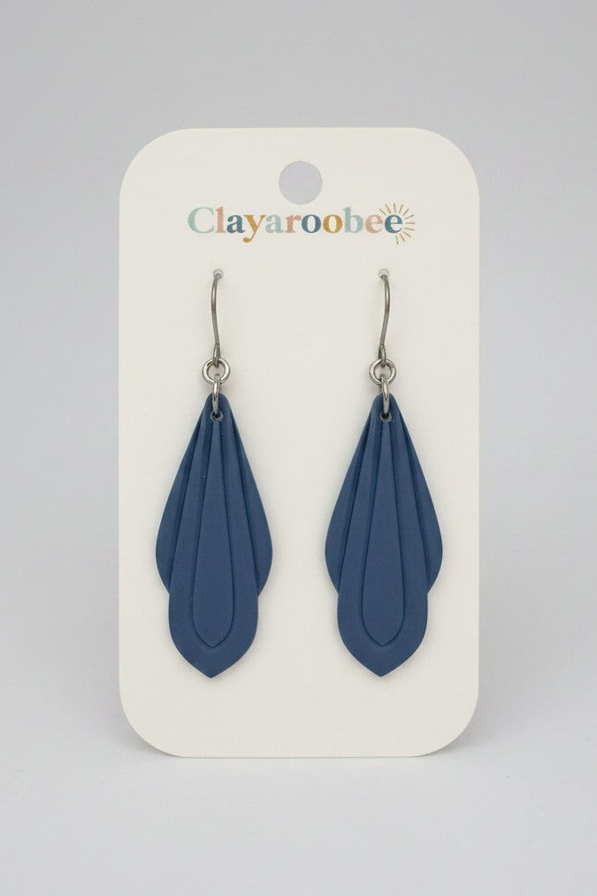 A pair of blue clay leaf-shaped dangle earrings on a white display card branded Clayaroobee