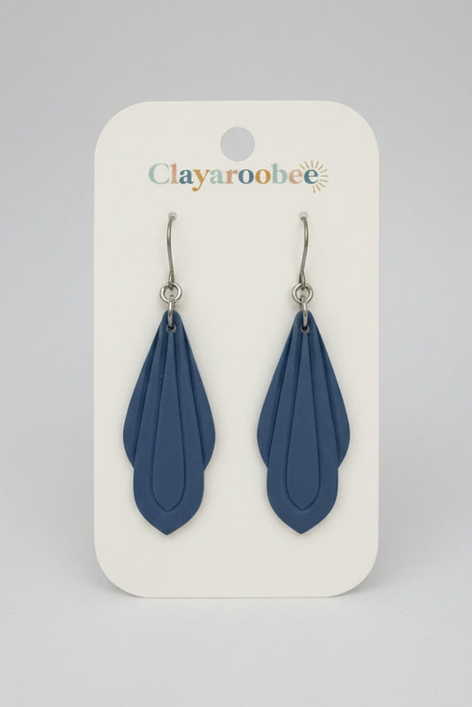 A pair of blue clay leaf-shaped dangle earrings on a white display card branded Clayaroobee