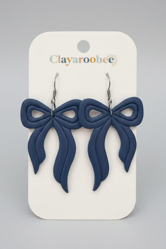 A pair of blue bow-shaped dangle earrings displayed on a white Clayaroobee brand card
