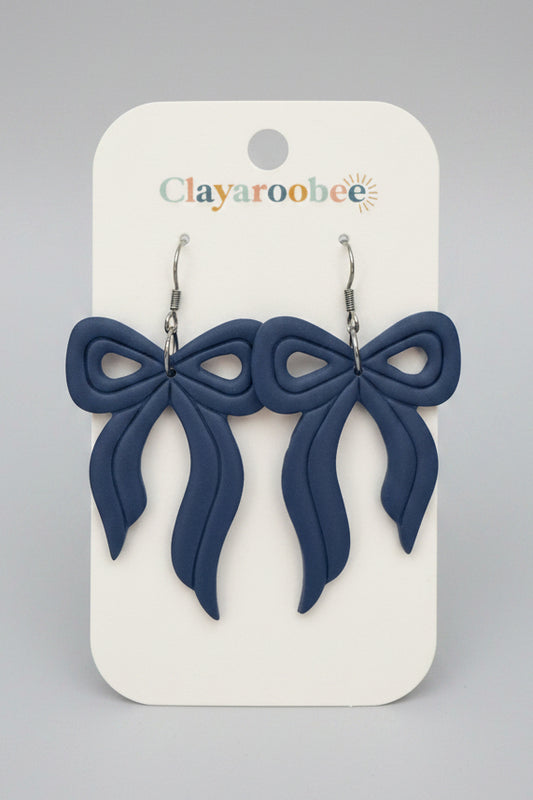 A pair of blue bow-shaped dangle earrings displayed on a white Clayaroobee brand card