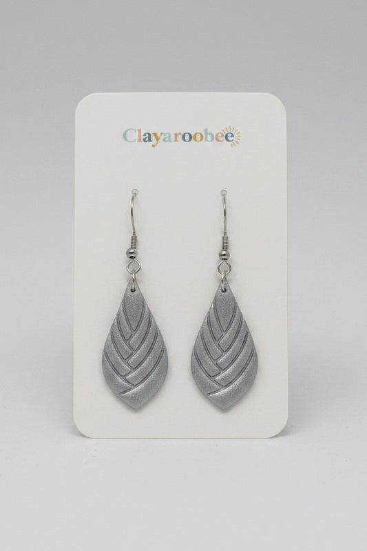 A pair of silver-toned teardrop dangle earrings with a layered leaf-like cutout design, displayed on a white Clayaroobee brand card. 