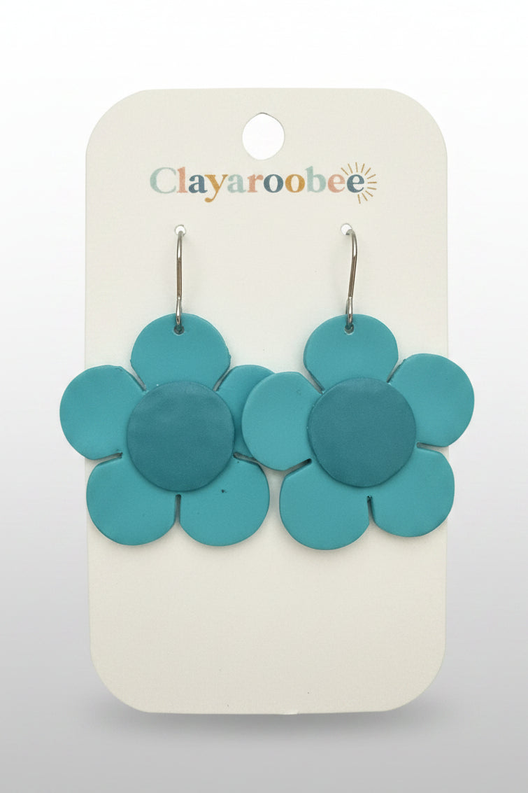 A pair of turquoise blue clay flower dangle earrings on a white display card with the Clayaroobee logo