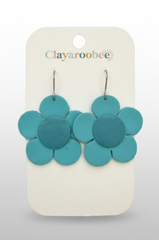 A pair of turquoise blue clay flower dangle earrings on a white display card with the Clayaroobee logo