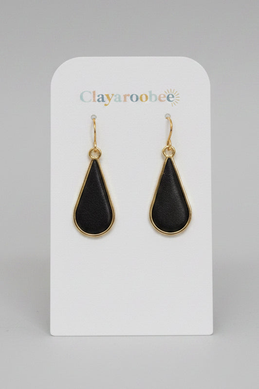 A pair of Clayaroobee teardrop-shaped drop earrings with black centers and gold-tone borders, displayed on a white brand card 