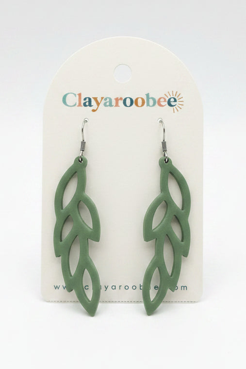 A pair of sage green leaf-shaped drop earrings displayed on a white Clayaroobee card