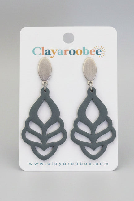 A pair of dark blue-gray leaf-shaped drop earrings with silver-toned studs, displayed on a white Clayaroobee brand card