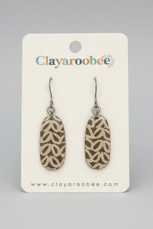 A pair of clay dangle earrings with a brown and beige geometric pattern, displayed on a white Clayaroobee brand card