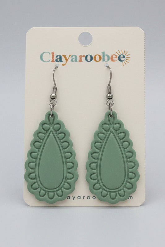 A pair of mint green clay earrings with a scalloped teardrop shape, displayed on a white Clayaroobee card. 