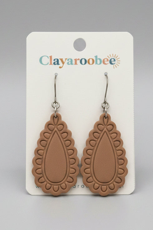 A pair of claydior teardrop-shaped drop earrings in a warm tan color, displayed on a white card labeled 'Clayaroobee' 