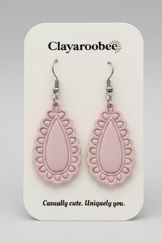 A pair of light pink teardrop-shaped dangle earrings with scalloped edges, displayed on a white brand card that reads 'Clayaroobee' 