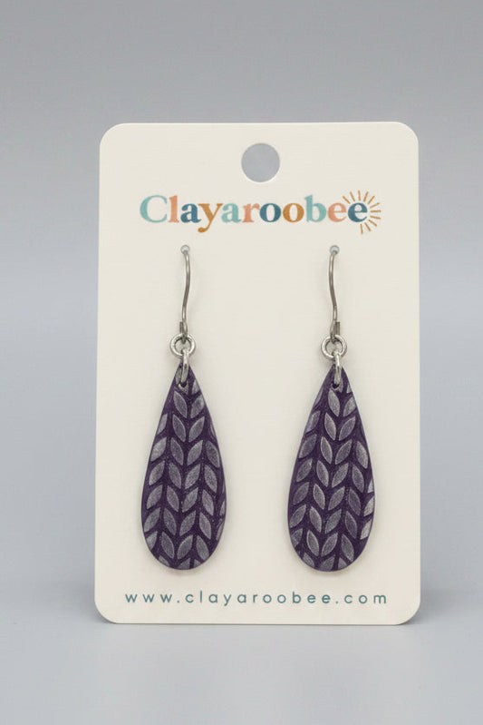 A pair of purple textured clay teardrop dangle earrings on a white Clayaroobee display card